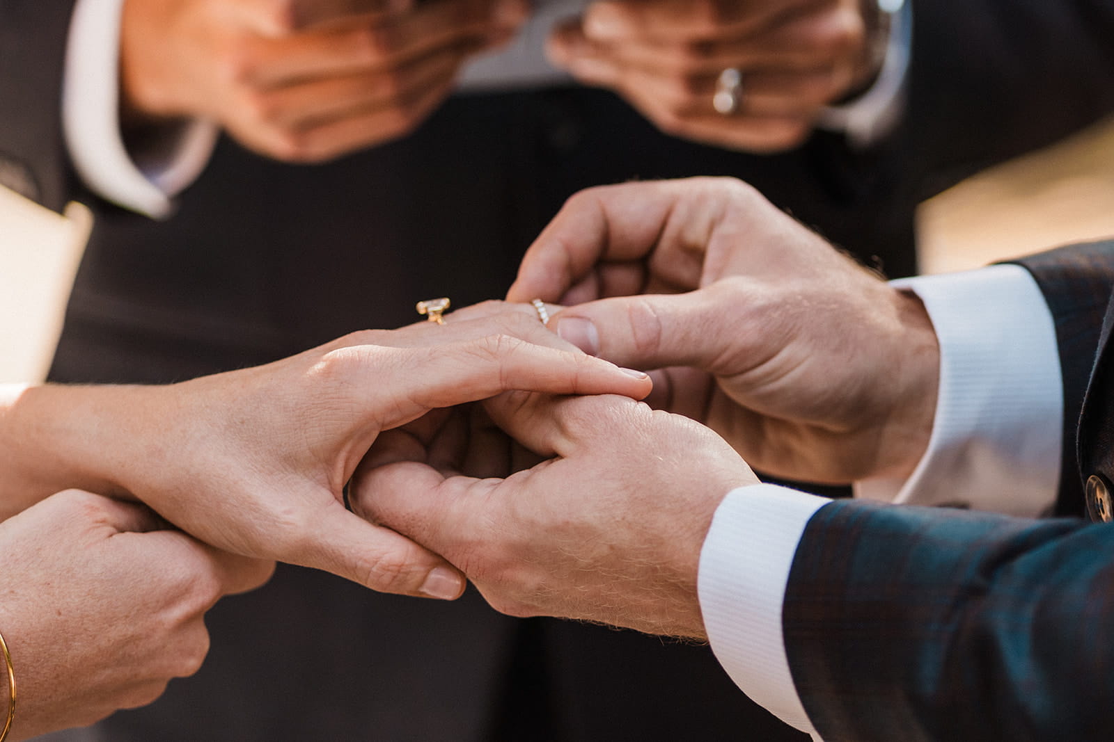 Groom places wedding band on bride's finger during their outdoor wedding ceremony. 