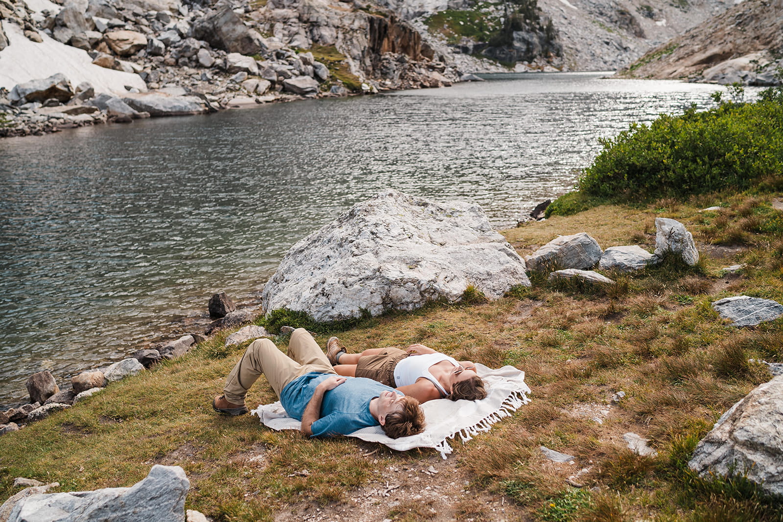Couple lays down on a picnic blanket next to an alpine lake to relax before their elopement.