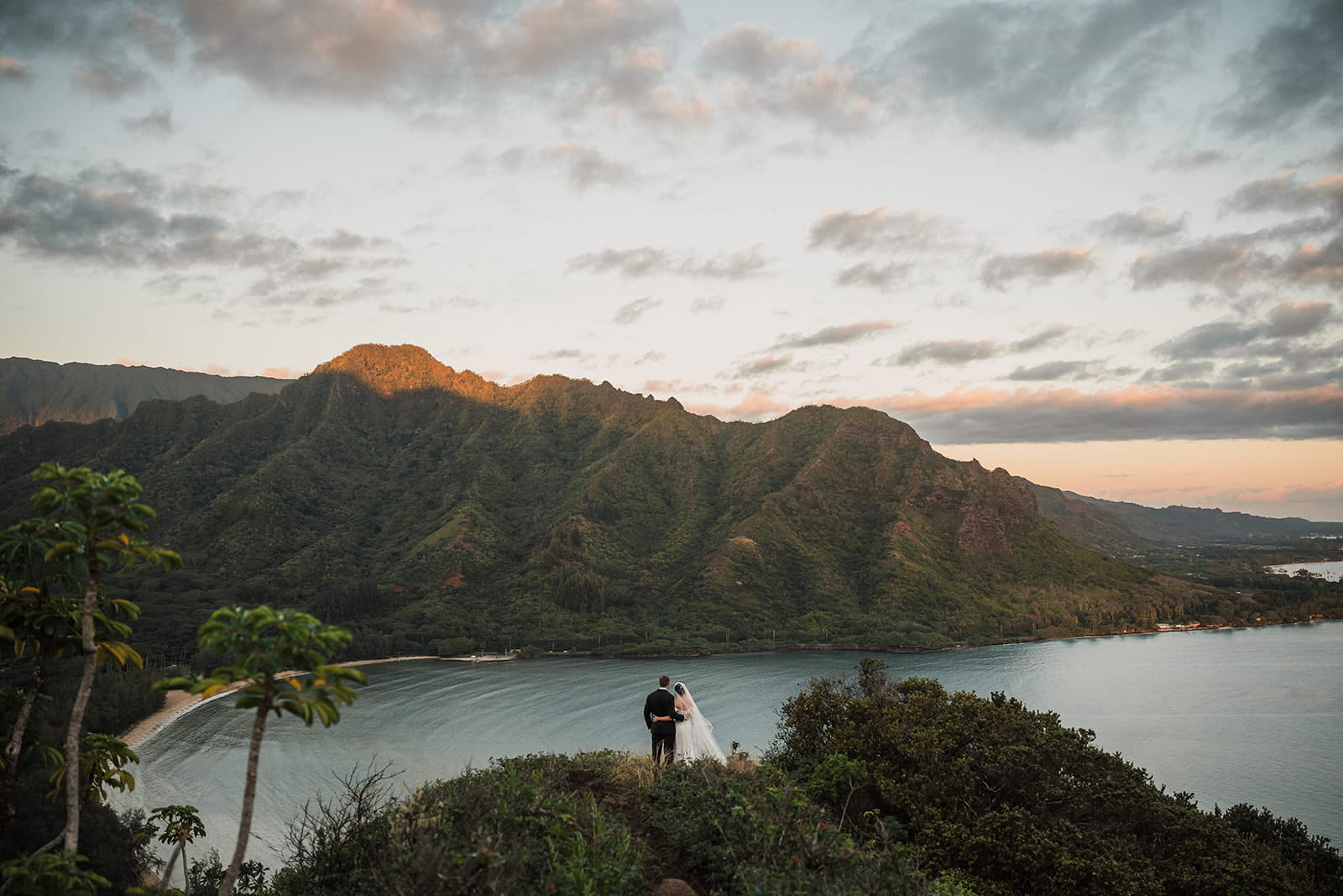 Newlyweds hug on a trail overlooking the ocean during their elopement photography session in Oahu.