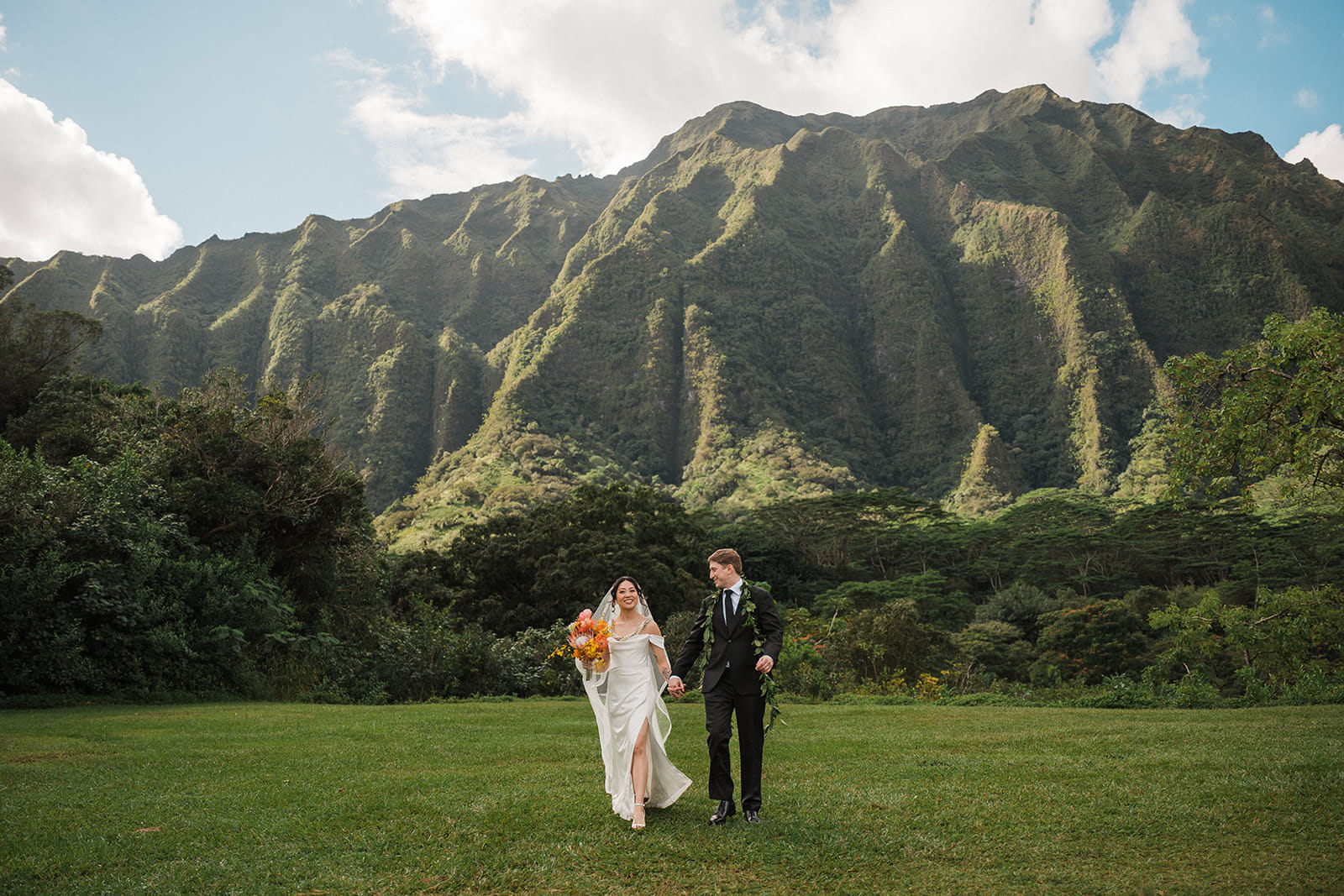 Newlyweds wander through a green field surrounded by mountains during their Kauai elopement.