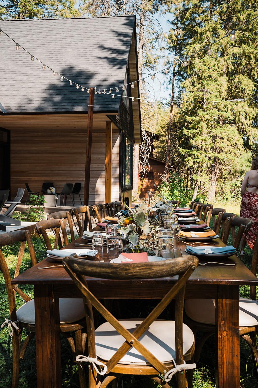 String lights hover above wood banquet tables at an outdoor reception at Apres Cabin.