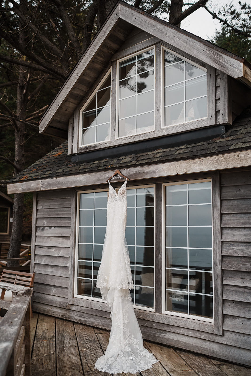 White lace wedding dress hangs from a coastal cabin at Crook Point, a micro wedding venue on the Oregon Coast.