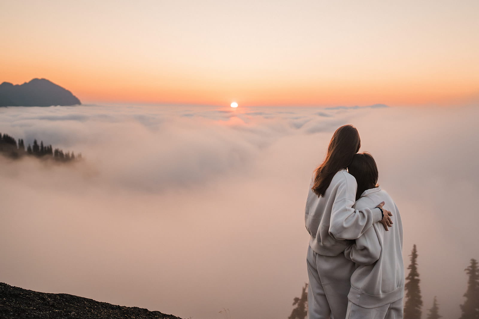 Two women hug while watching the sun rise above the clouds at Hurricane Ridge.