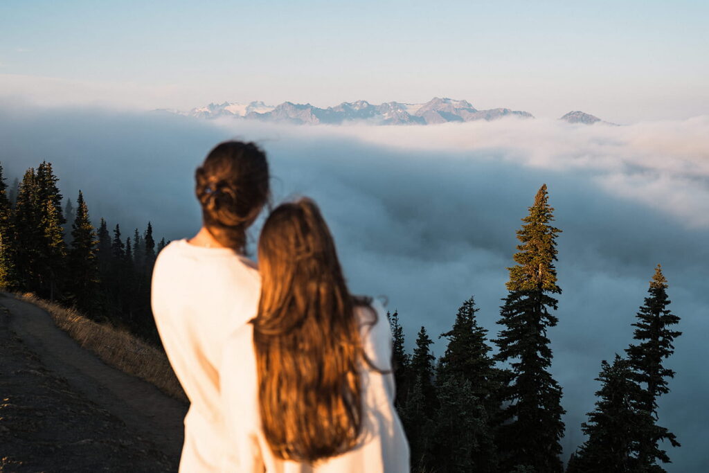 Two women watch the sunrise above the clouds at Hurricane Ridge.