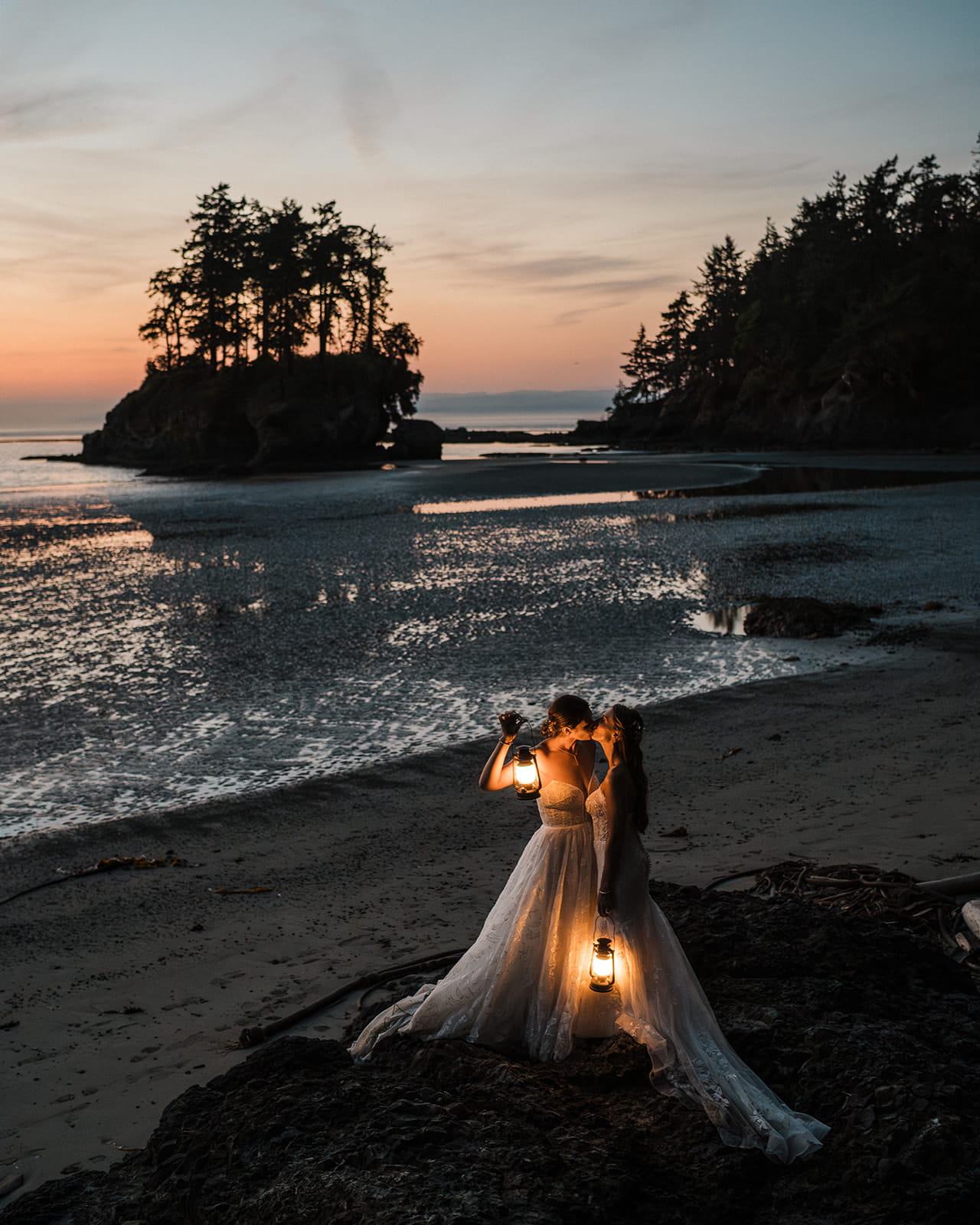 Brides kiss while holding lanterns on the beach on the Olympic Coast.