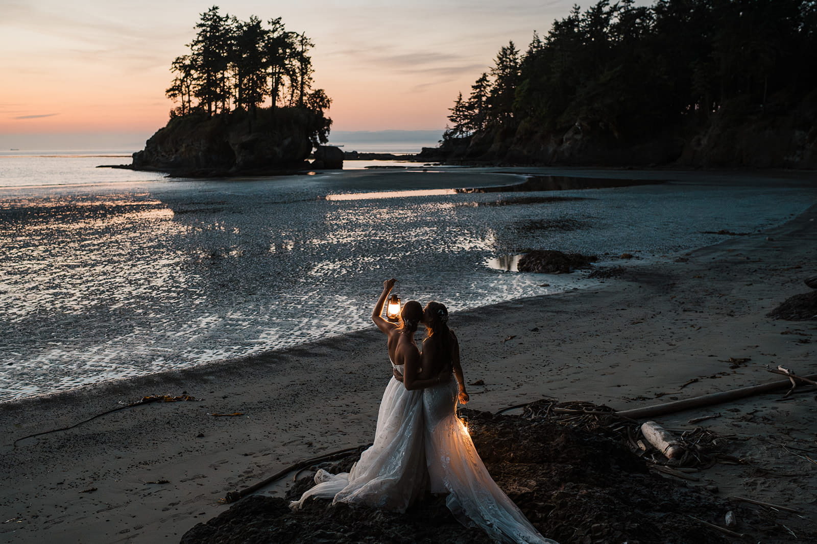 Two brides kiss while holding lanterns on the beach at blue hour during their Port Angeles beach wedding.