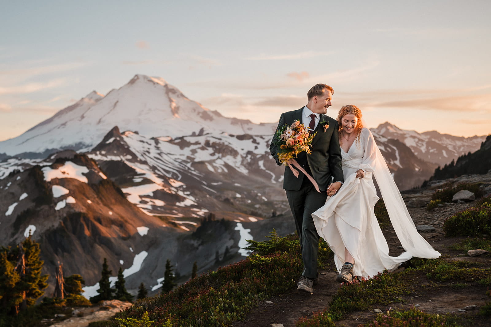 Bride and groom walk a mountain trail during sunset in the North Cascades.