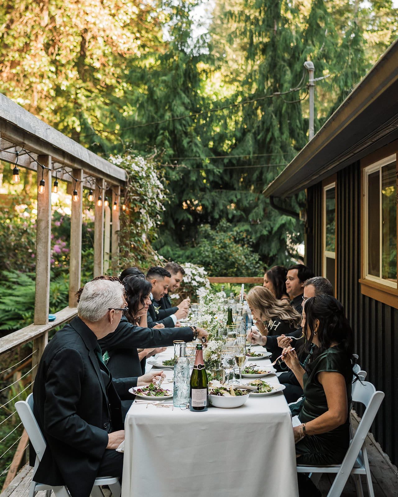 Guests sit at a rectangle table on an Airbnb deck for an intimate elopement reception dinner. 