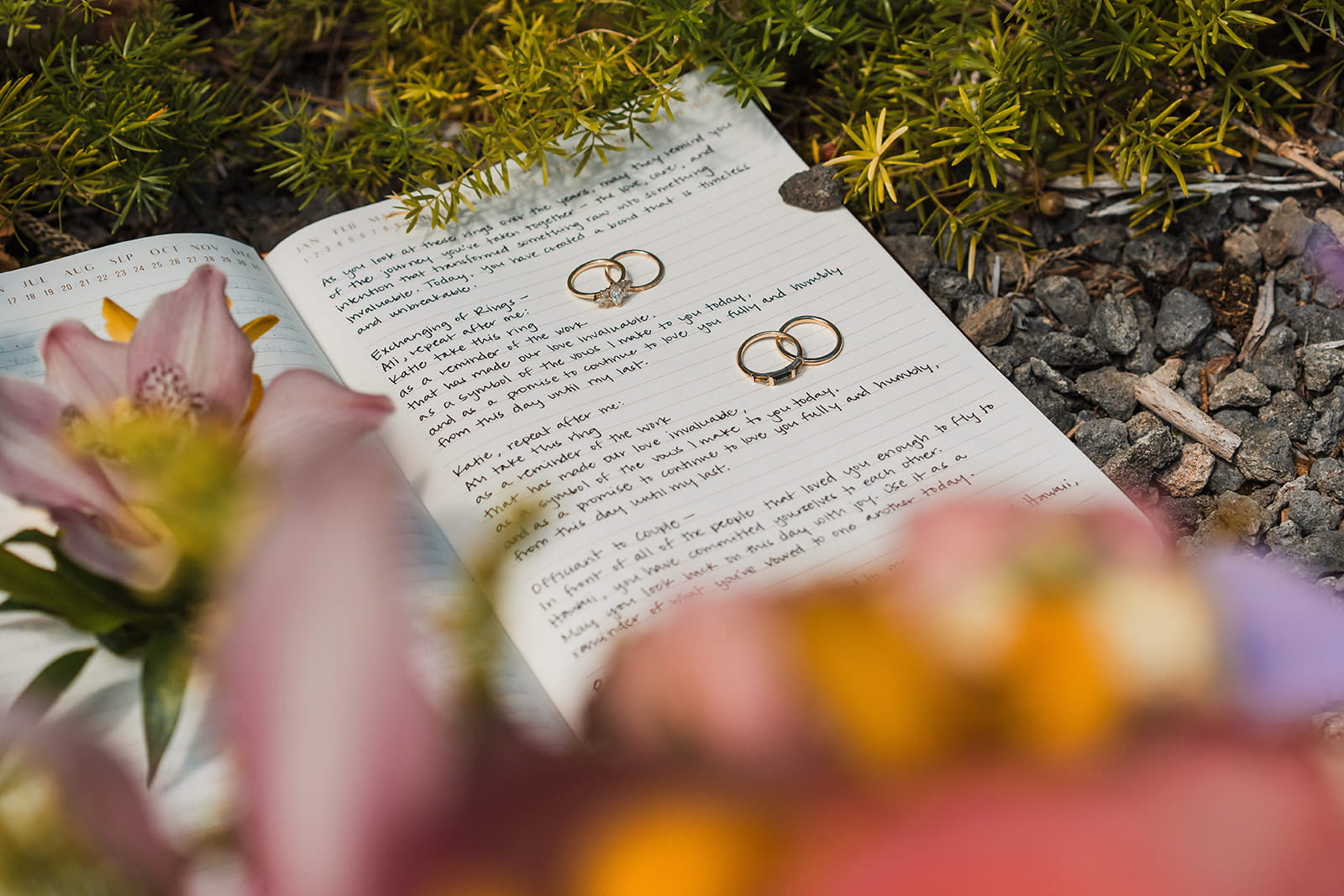 Wedding rings lay on a personal vow book with wedding flowers.