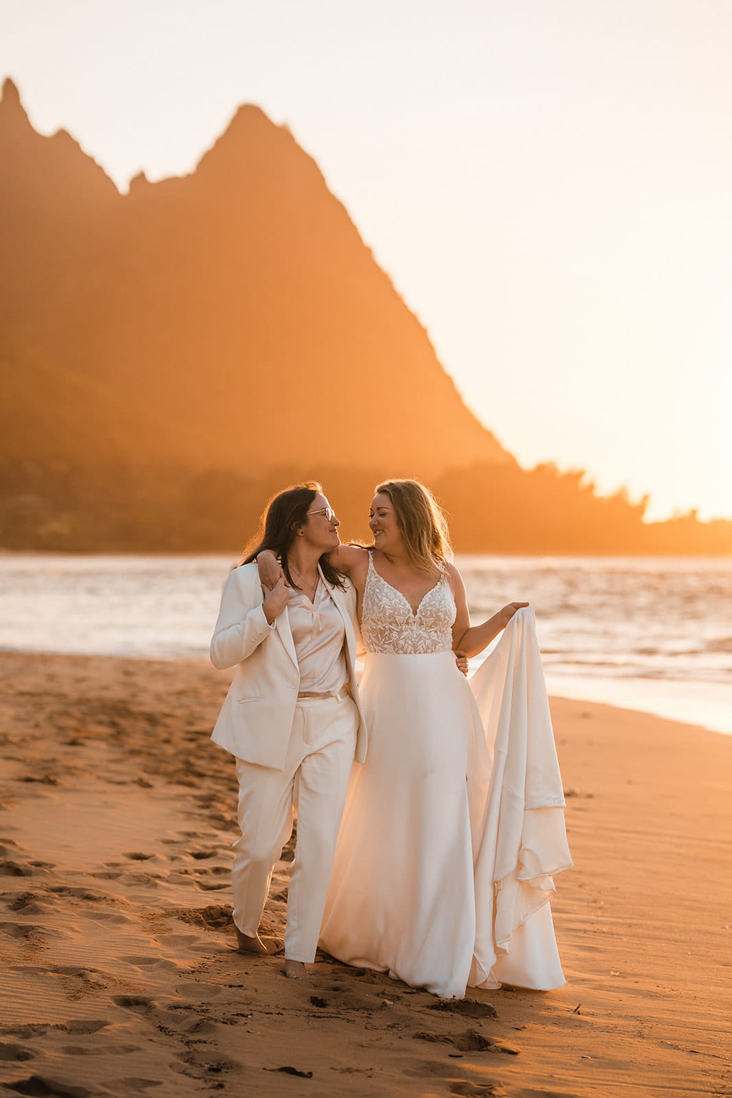 Two brides walk across Tunnels Beach during their two-day Kauai beach wedding.